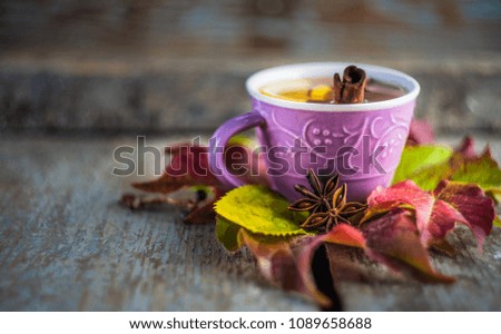Autumnal concept with cup of tea with lemon, cinnamon stick and anise star on rustic wooden  background full of bright yellow leaves