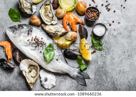 Raw fish Dorado and fresh seafood oysters, shrimps, clams, mussels, shells with lemon, olive oil, herbs on grey stone rustic background, top view. Ready for cooking seafood, close-up Royalty-Free Stock Photo #1089660236