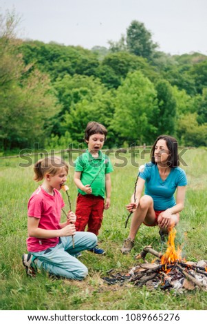 Family picnic. Children with their mother fry marshmallows on skewers. Family holiday in nature. A boy with his parents and brother bake marshmallows on fire.