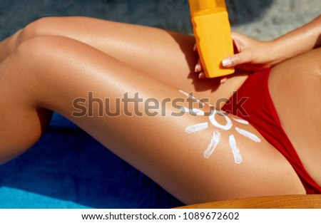 Woman sunbathing on the beach. Close-up view on the legs with lotion sun shape 