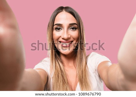 Young pretty woman smiling and happy, taking a selfie, holding the camera, excited by his vacation or by an important event, cheerful expression