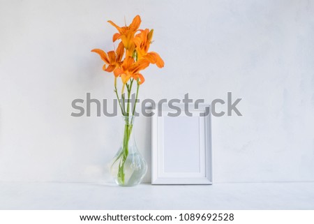 Mockup with a white frame and orange summer flowers in a vase on a light background