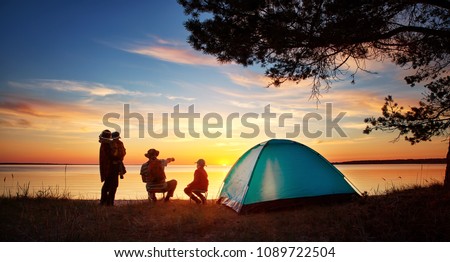Family resting with tent in nature at sunset. Woman, man and children near seaside