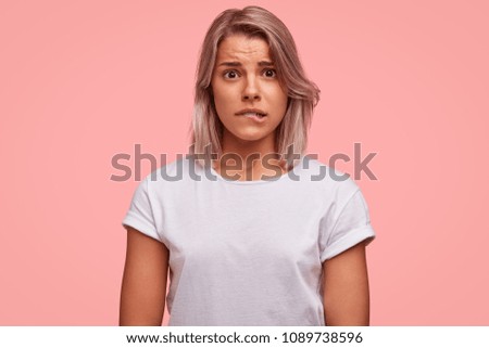 Portrait of discontent female curves lips, feels nervous before making inportant decision, has frustrated expression, wears casual white t shirt. People, emotions, facial exressions concept.