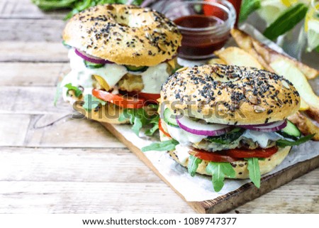 Homemade chicken bagel burger with cheese, arugula, tomato and onion on wooden table. Selective focus