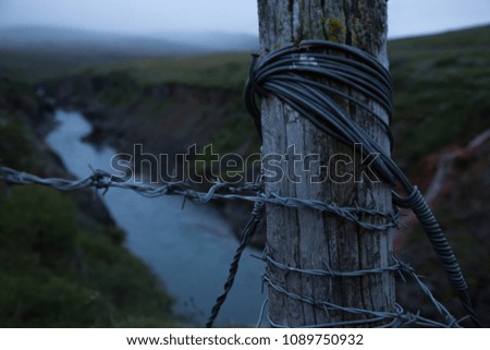 Barbed wire on a fence and river flow in the background at twilight.