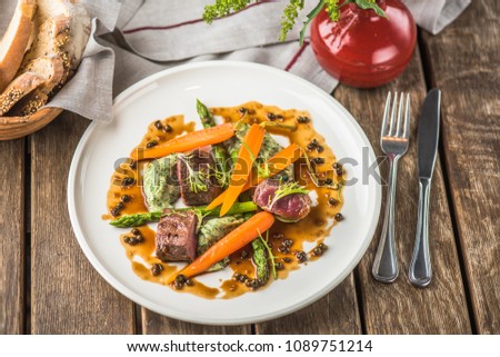 Meat fillet and vegetables in sauce, a glass of wine and flowers. Healthy fresh food on a wooden table.