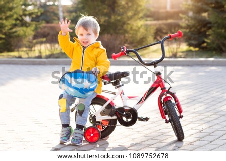 Three years old child boy in safety helmet riding on a bicycle at cobbles road in the city park in spring or summer. Happy childhood and kids first trip on a four-wheeled bicycle