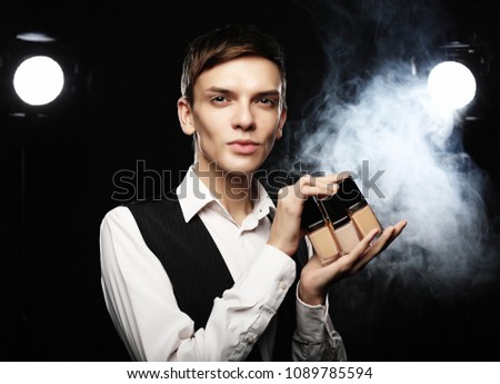 Beauty concept. Young male make up artist posing  with foundation for make-up on a dark background.