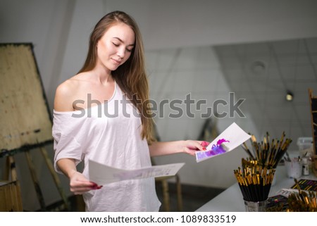 Young artist teacher comparing sheets with color samples her before classes at art school.