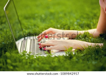 The laptop is on the grass and female hand close-up