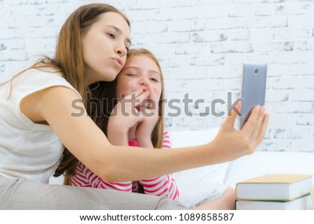 Mom and daughter giving kiss to the mobile phone screen while video calling with dad.