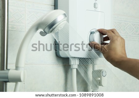 Hand regulate the temperature of hot water in electric water heater Royalty-Free Stock Photo #1089891008