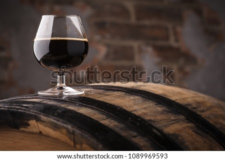 Snifter glass with black stout beer standing on an oak barrel in a cellar Royalty-Free Stock Photo #1089969593