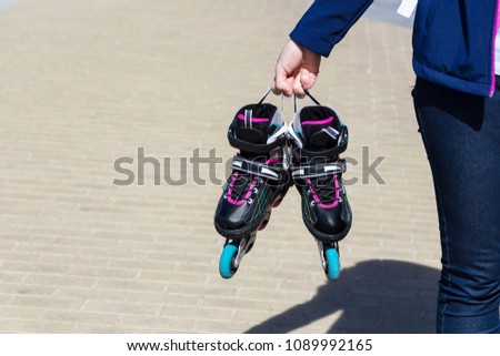 Closeup of a girl holding a roller skate. On the background of paving slabs.