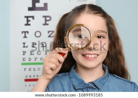 Cute little girl with magnifier in ophthalmologist office