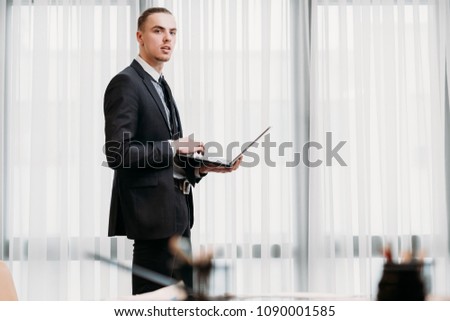 business man lifestyle. young handsome male in formal clothing standing in office holding laptop. elegant successful corporate manager workspace