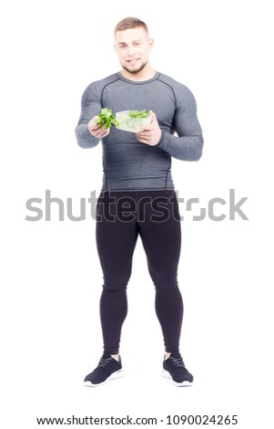 Full-length portrait of well-muscled male athlete holding lunch box with fresh celery