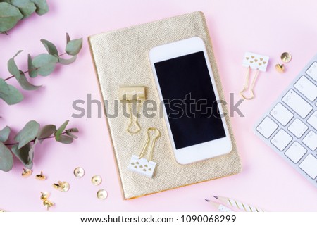 Home office desk with green eucaliptus and modern white phone on pink background