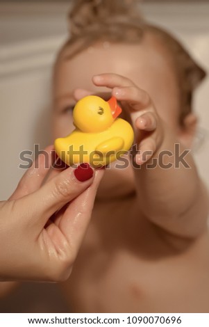 Little child sitting in bathroom with wet hair taking yellow duckling toy from hand of mother, vertical picture