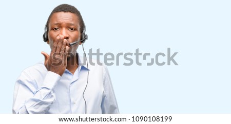 Black man consultant of call center covers mouth in shock, looks shy, expressing silence and mistake concepts, scared
