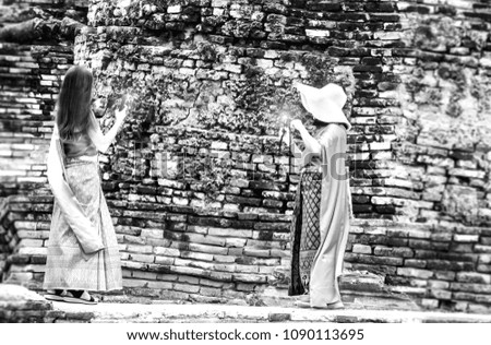 Black and white photo of female tourists dressed in Thai dress and taking photos.