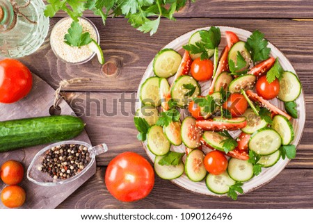Vegetable salad of fresh cucumbers, tomatoes, parsley and sesame seeds on a plate on a wooden table. Ingredients for salad preparation. Top view