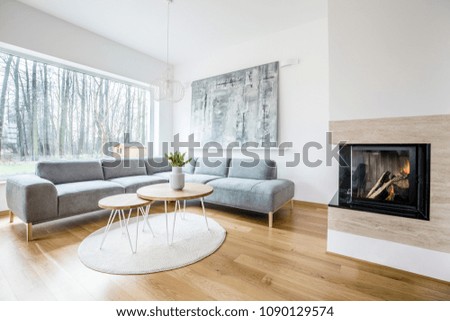 Wooden table on a round rug near sofa in spacious living room interior with fireplace and painting