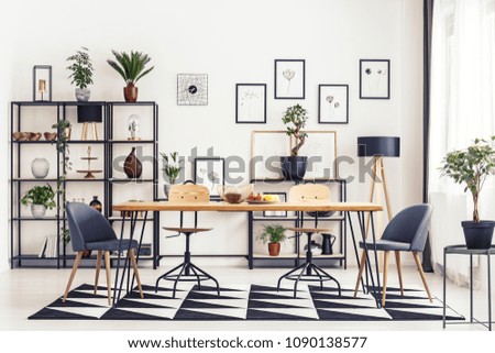 Grey chairs at table on black and white carpet in dining room interior with gallery of posters