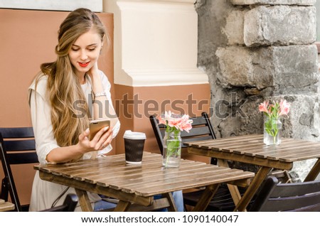 Portrait of a smiling bussines casual woman holding smartphone drinking coffee with long hair in cafe city street sunny day background