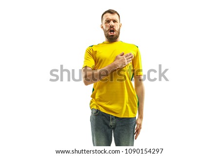 Brazilian fan celebrating on white background. The young man in soccer football uniform standing and singing a hymn at white studio. Fan, support concept. Human emotions concept. Royalty-Free Stock Photo #1090154297