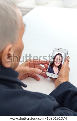 Senior person sitting with her smartphone at a table looking at a photo of her beloved granddaughter, modern lifestyle concept