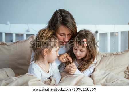 Mom and two daughters draw in bed in the bedroom