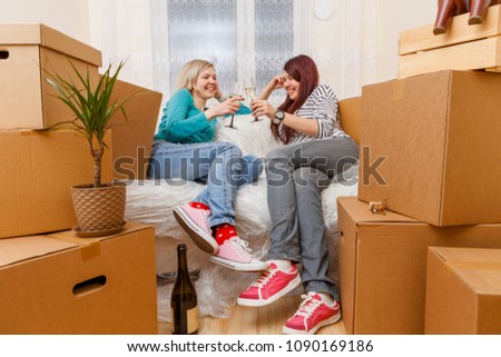 Photo of two girls sitting on sofa among cardboard boxes