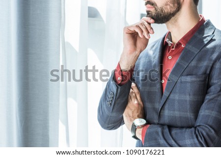 cropped shot of young businessman with hand on chin looking through window