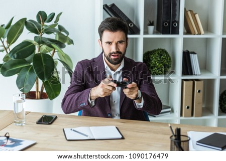 handsome young businessman with gamepad looking at camera while sitting at workplace