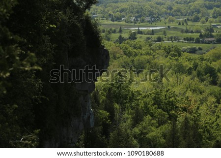 Image looking out over the edge of a cliff with part of the plateau on the left and the forest and farmland stretching out into the distance on the right.