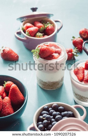 Strawberry cheesecake inside glass jar over a blue background and  top view of berries , inside ceramic colored cocotte, blueberries, strawberries, raspberries, flat lay