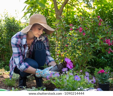 Beautiful female gardener holding a flowering plant ready to be planted in her garden. Gardening concept.