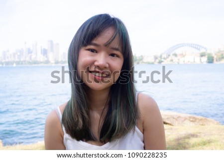 Young woman sits on the background of the beautiful Sydney skyline on a sunny day in a white dress and sunglasses