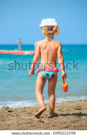  One little girl walk on the beach with spades. Bright summer time.