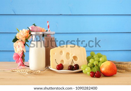 image of fruits and cheese in decorative basket with flowers over wooden table. Symbols of jewish holiday - Shavuot