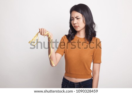 Unhappy young Asian woman with measuring tape on white background
