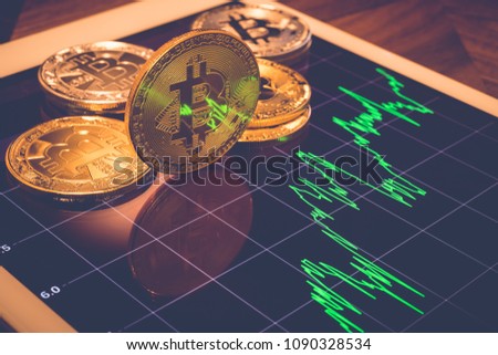 Cryptocurrency gold metal, focus bitcoin sign on tablet screen that showing light reflex of green price or stock market performance graph, vintage filter. Concept of exchange money through blockchain.
