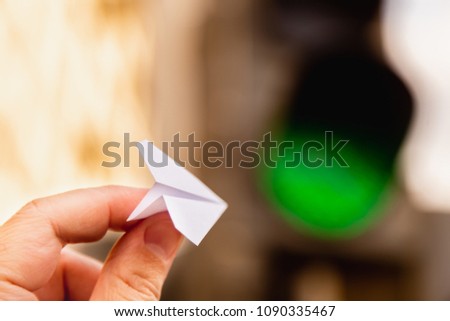 One small paper airplane in hand against a traffic light background with a glowing green signal. Permission to fly. Takeoff is approved and allowed. Horizontal frame. Concept Royalty-Free Stock Photo #1090335467