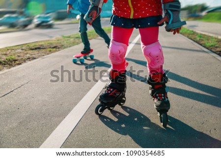 little gilr on roller skates and boy on skateboard outside