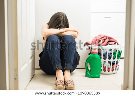 Upset young woman feeling frustrated sitting on laundry room floor