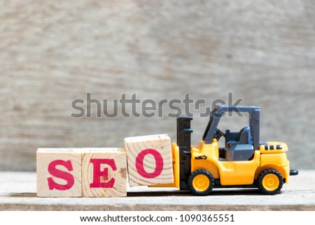 Toy forklift hold letter block O to complete word SEO (abbreviation of Search Engine Optimization) on wood background