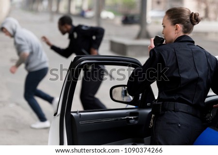 policewoman talking by radio set while her partner chasing thief Royalty-Free Stock Photo #1090374266