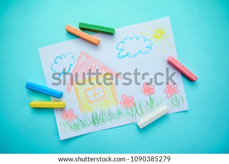 Children's drawing with colored chalks with a house, grass, flowers and clouds on a blue background